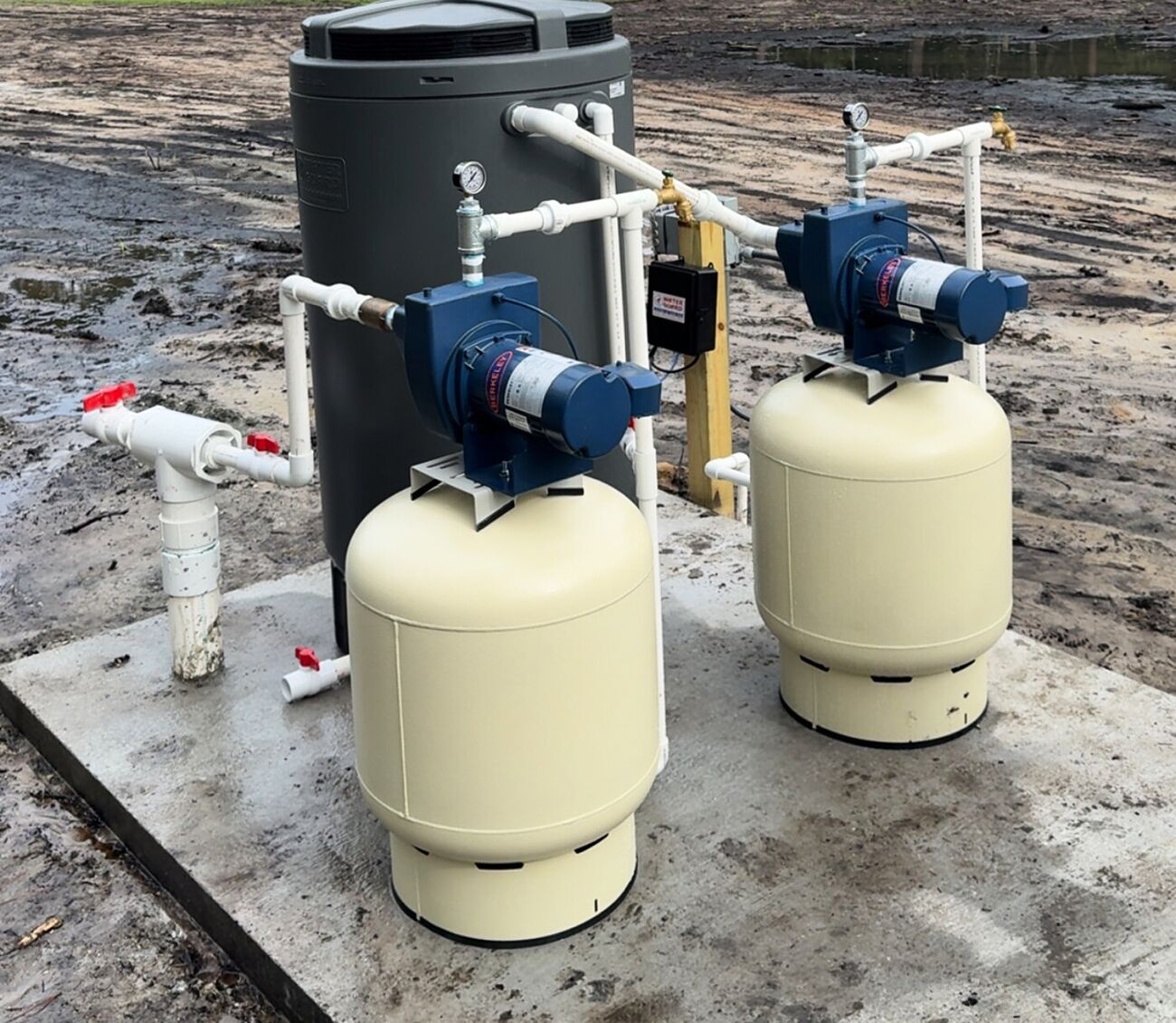 A twin-pump water system on a concrete pad with two pressure tanks, a storage tank and a valve manifold